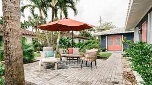 Una zona patio con mobili da esterno, un ombrellone rosso e una casa con una porta rossa.