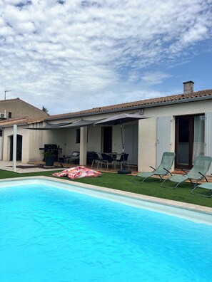 A residential property with a swimming pool, outdoor seating, and a covered patio.