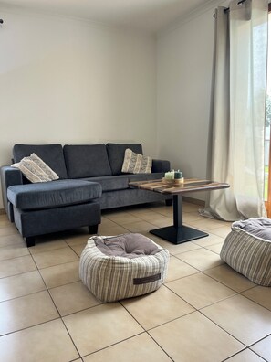A living room with a grey sofa, a wooden coffee table, and two patterned ottomans.