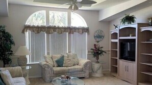 A living room with a ceiling fan, a sofa, a coffee table, and a TV stand.