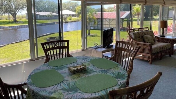 A sunroom with a view of a lake, a ceiling fan, and wicker furniture.