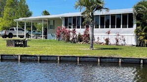 A house with a covered porch, a swimming pool, and a lawn with palm trees.