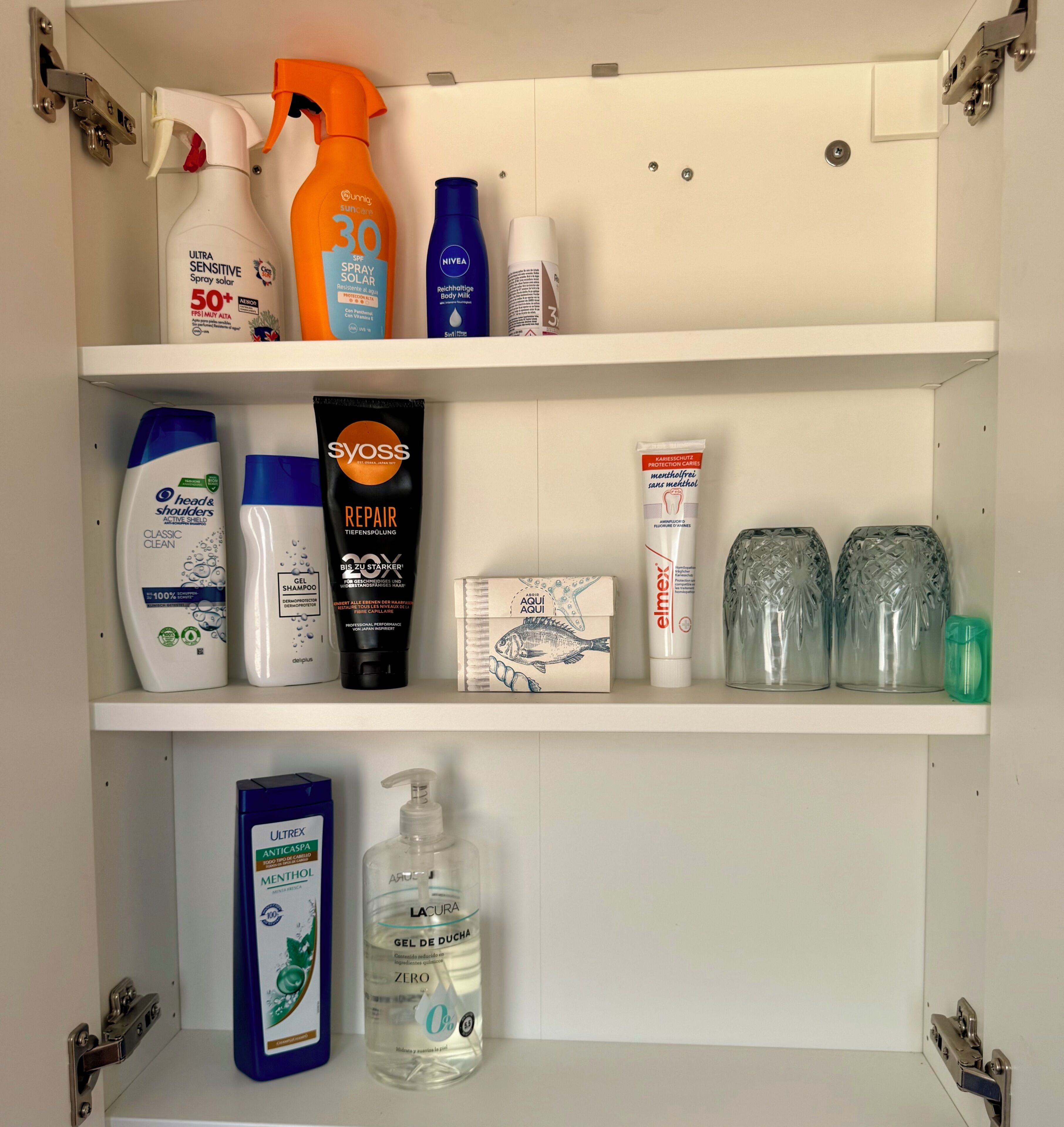 En hylla i badrummet med olika hygienartiklar, inklusive en flaska solskyddsmedel, duschkräm, schampo och en flaska hårgelé.