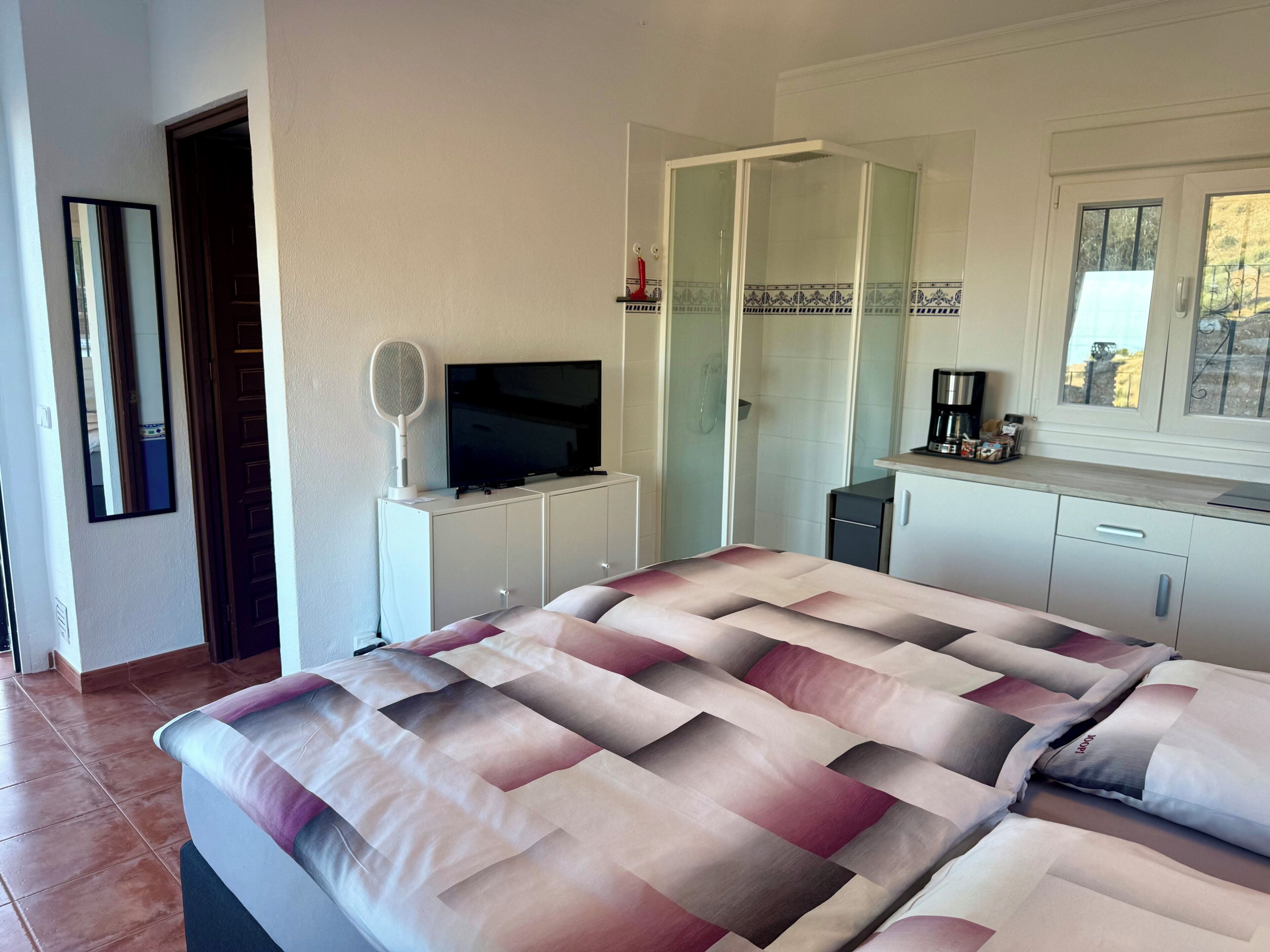 Ein Hotelzimmer mit einem Bett, einem Fernseher, einem Spiegel, einer Dusche und einem Fenster.
