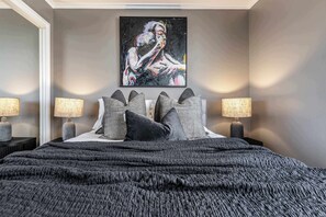 Een moderne slaapkamer met een groot bed, twee bedlampen en een schilderij aan de muur.