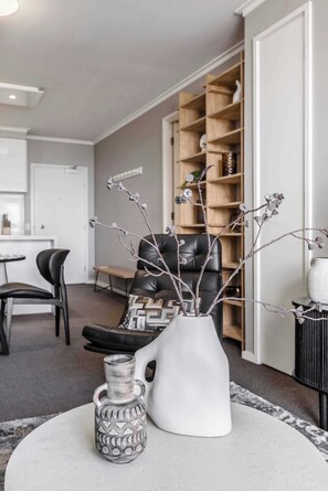 Een woonkamer met een witte vaas, een keramieken object met een patroon en een zwarte leren fauteuil.