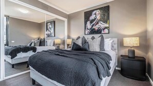 Ein Schlafzimmer mit einem großen Spiegel, einem Bett mit schwarz-weiß gestreifter Bettdecke, einem Nachttisch mit Lampe und einem Bild an der Wand.