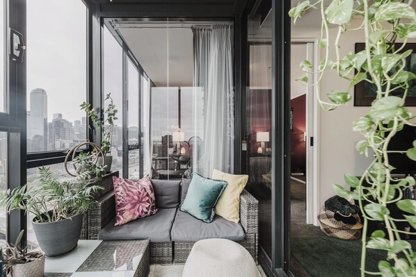 Ein Balkon mit einer Couch, Kissen, Blumentöpfen und Blick auf die Stadtlandschaft.