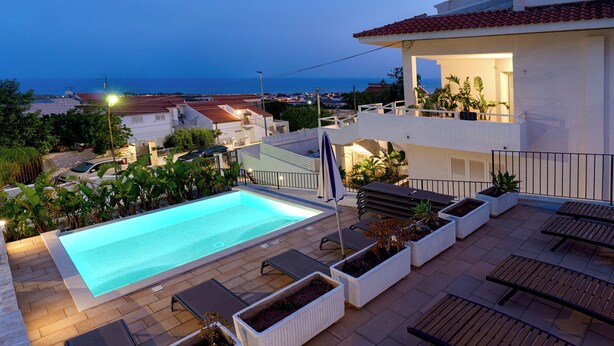 Un área de piscina en la azotea con sillones de descanso, plantas en macetas y vista al mar.