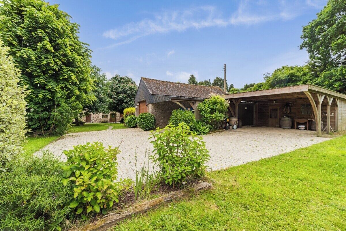 A rustic stone house with a covered porch and a gravel driveway.