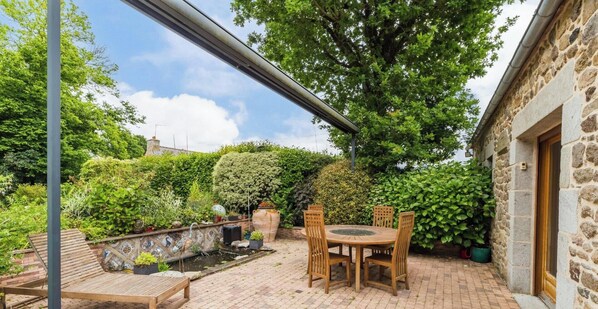 Une terrasse avec une table et des chaises, entourée d’une végétation luxuriante et d’un mur de pierre.
