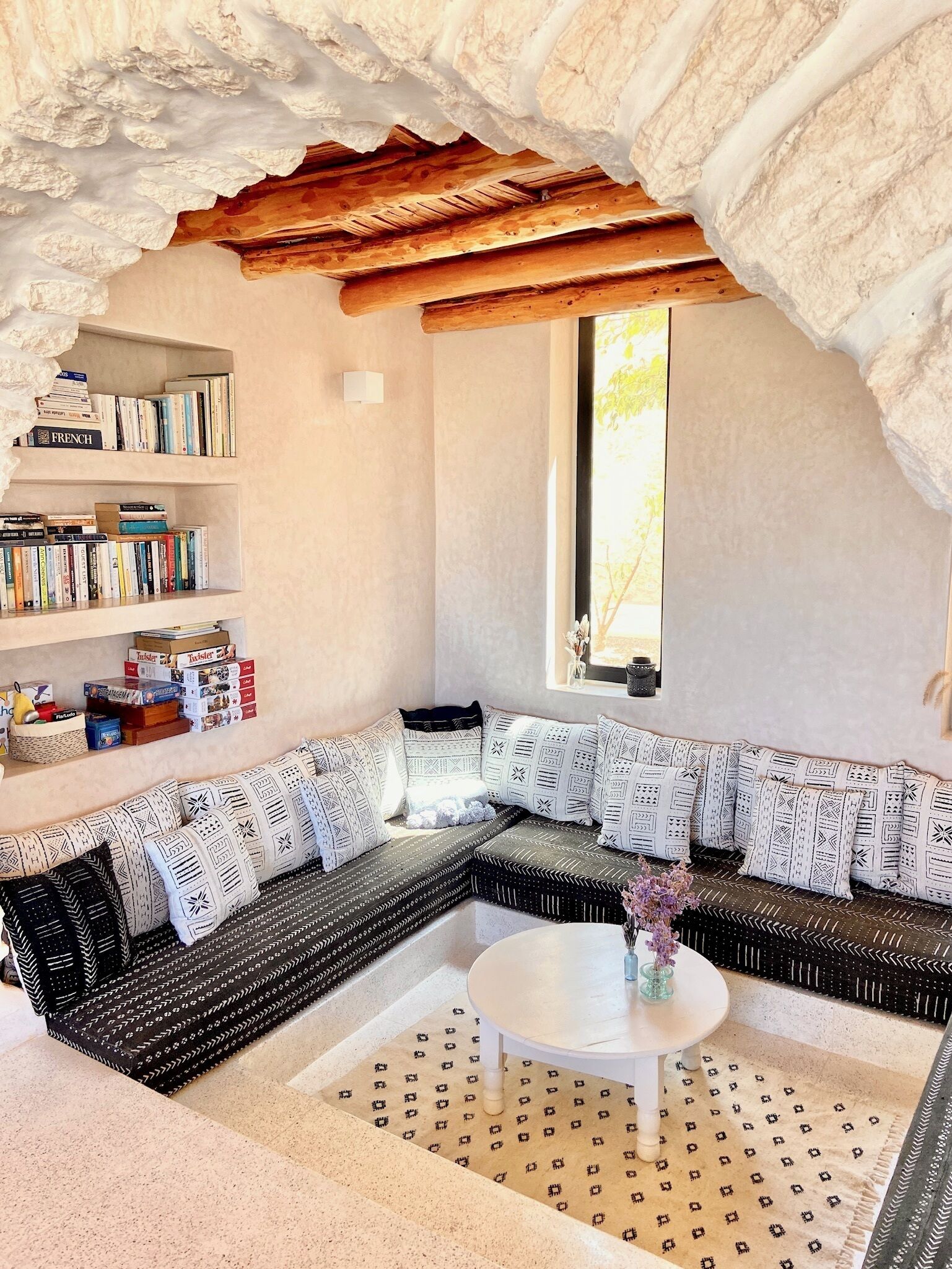 A cozy living room with a sectional sofa, a coffee table, and a bookshelf filled with books.