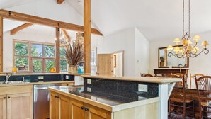 Eine geräumige Küche mit Holzbalken, einer Arbeitsplatte aus Granit und einem Essbereich mit einer Chandelüster.