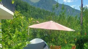 A tent set up in a grassy area with a table and chairs, surrounded by greenery and mountains in the background.