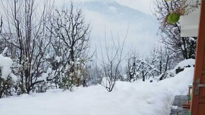 A snow-covered pathway leading to a building with a view of snow-covered trees and mountains in the background.