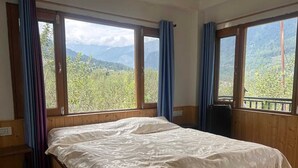 A bedroom with a wooden bed, large windows, and a view of a mountainous landscape.