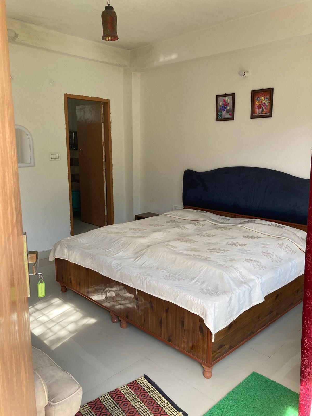 Een slaapkamer met een houten bed, een nachtkastje, een groen kleed en twee ingelijste foto's aan de muur.