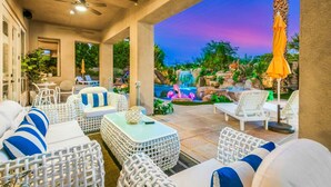 Un espace extérieur aménagé, abrité et doté de mobilier en osier, une piscine avec une cascade et une vue imprenable sur le coucher de soleil.