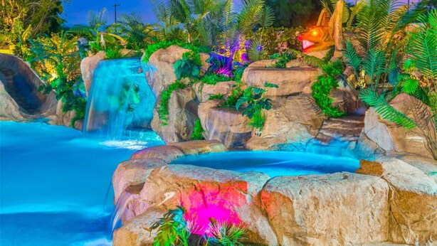Un jardin tropical avec une cascade, des rochers et différentes espèces de plantes.