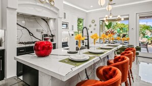Une cuisine moderne avec un plan de travail en marbre, un saladier décoratif rouge et des chaises orange.