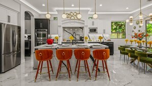 Une cuisine moderne dotée d’un îlot central, d’appareils électroménagers en acier inoxydable et d’un coin repas avec des chaises vertes et une table.