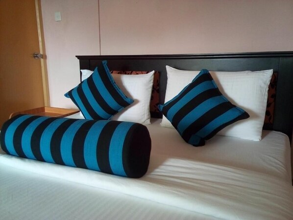 A bed with white linens, two pillows with blue and black stripes, and a wooden headboard.