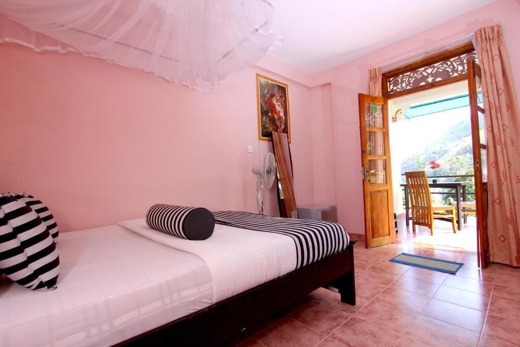A bedroom with a bed, a fan, a door leading to a balcony, and a view of the outdoors.
