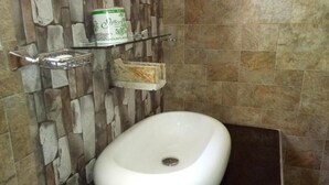 A bathroom with a white sink, a stone wall, and a shelf with a soap dispenser. - Blue Ribbon Homestay  (Ella)