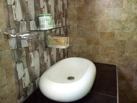 Une salle de bain avec un lavabo blanc, un mur en pierre et une étagère sur laquelle se trouve un distributeur de savon.