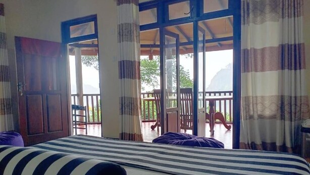 A room with a bed, curtains, and a balcony with chairs. - Blue Ribbon Homestay  (Ella)
