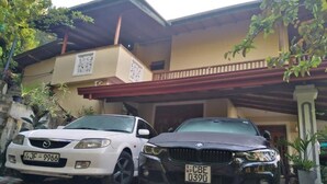 Two cars parked in front of a building with a balcony and a tiled entrance. - Blue Ribbon Homestay  (Ella)