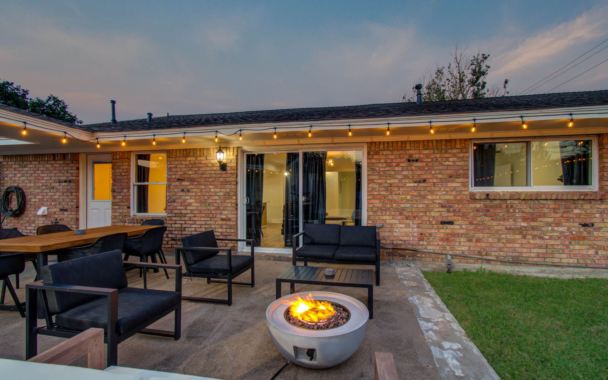 Un patio al aire libre con un brasero, asientos e iluminación con luces colgantes.