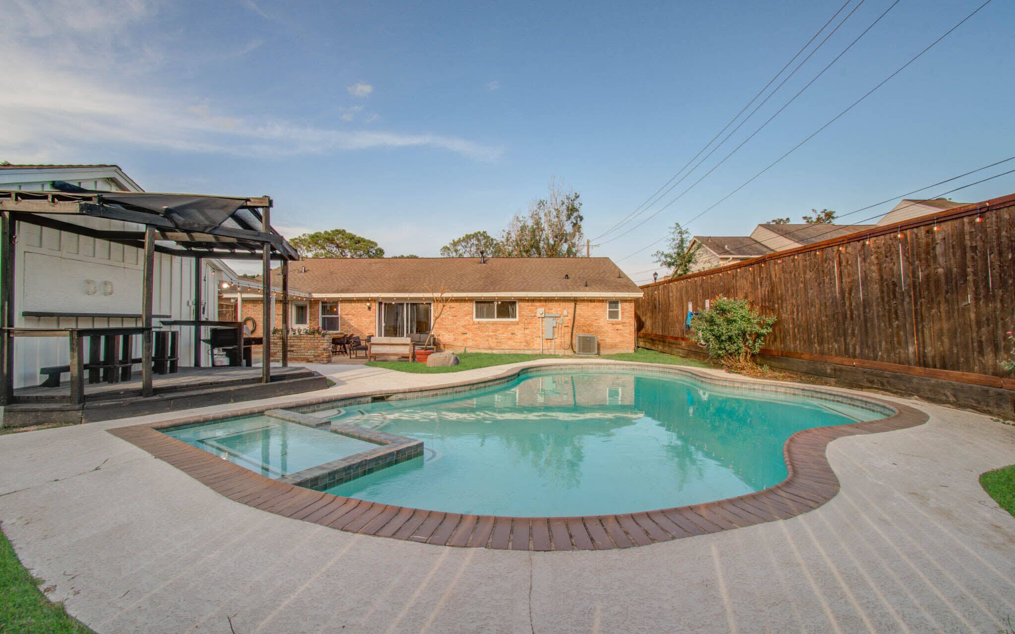 Ein Garten mit Swimmingpool, einer überdachten Terrasse und einem Ziegelhaus.