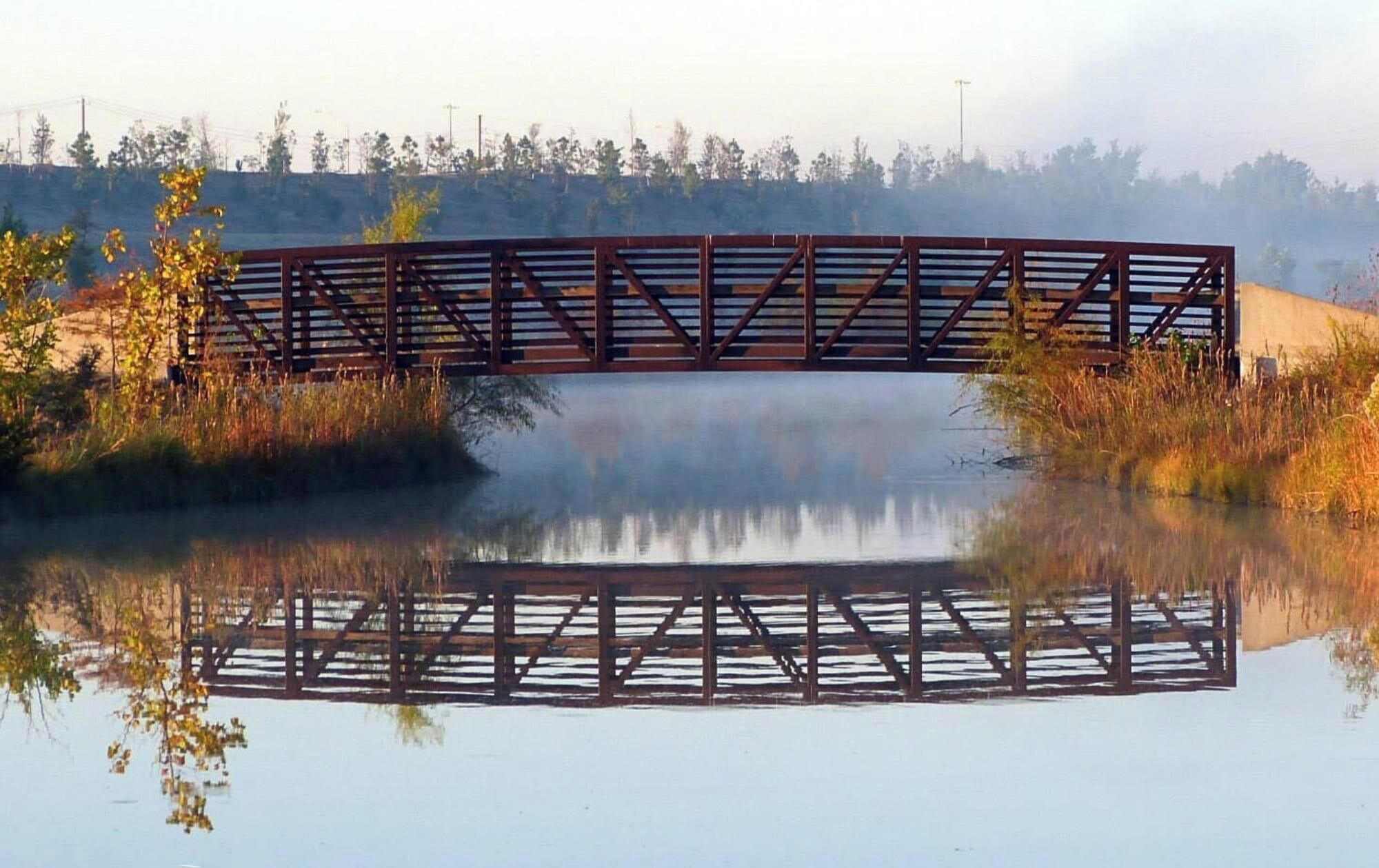 Eine Metallbrücke über stillem Wasser, mit deutlicher Spiegelung.