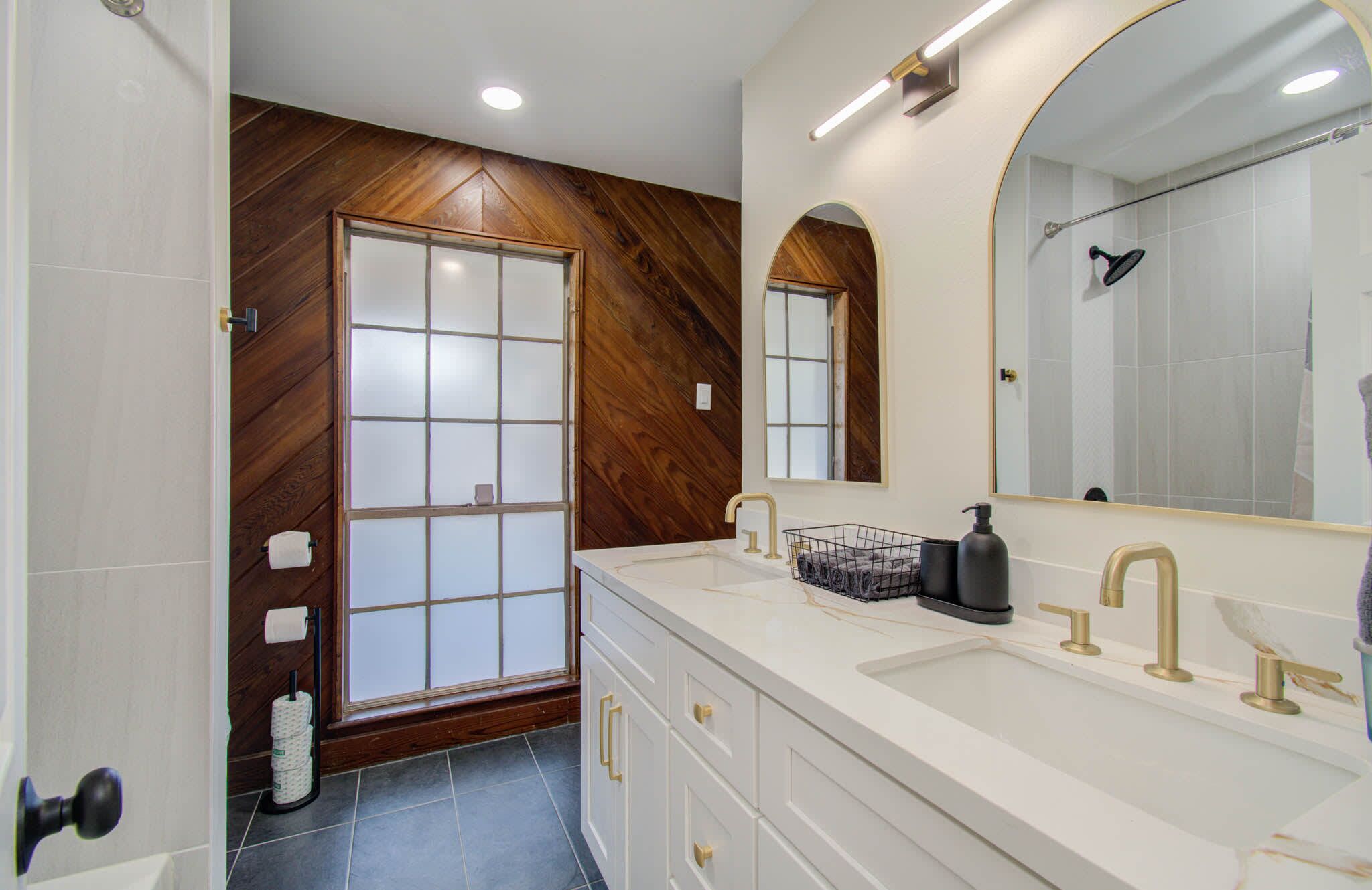 A modern bathroom with a wooden accent wall, a large mirror, and a dual sink vanity.