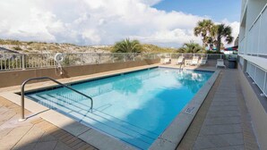 A rectangular swimming pool with a metal ladder, surrounded by a white fence. There are lounge chairs and umbrellas on the right side.