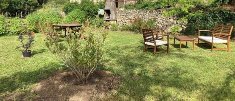 A stone house with a tiled roof, a small garden with a wooden table and chairs, and a potted plant.