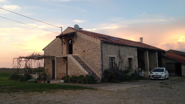 A stone building with a red-tiled roof, a satellite dish, and a car parked in front.