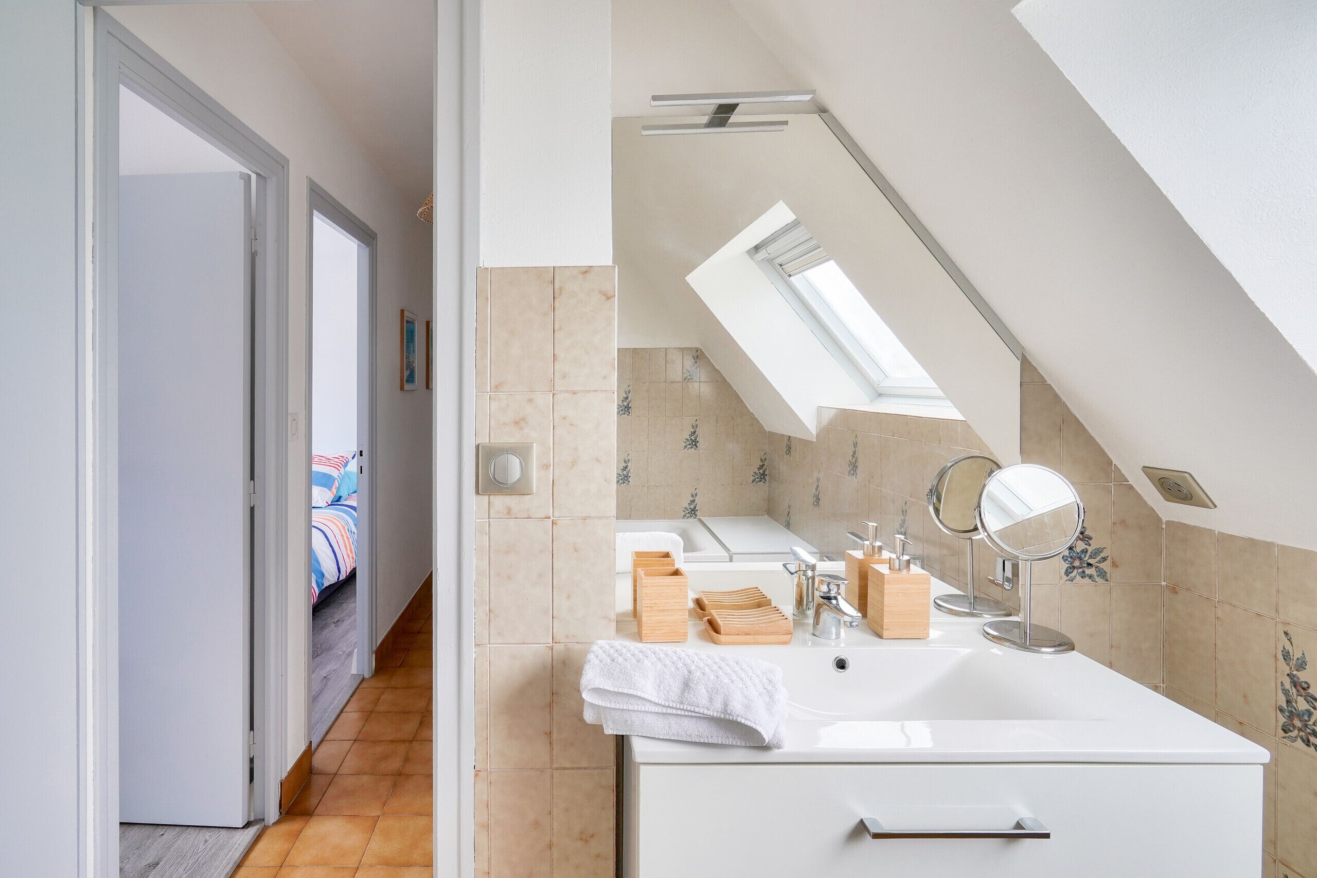 A modern bathroom with a skylight, a white sink, and wooden towel holders.