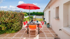 Une terrasse extérieure avec une table et des chaises, un parasol rouge et une haie.