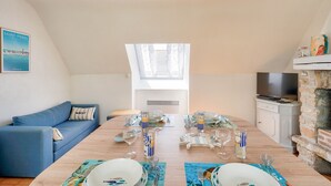 Un coin repas avec une table en bois dressée pour quatre personnes, un canapé bleu et une cheminée en pierre.
