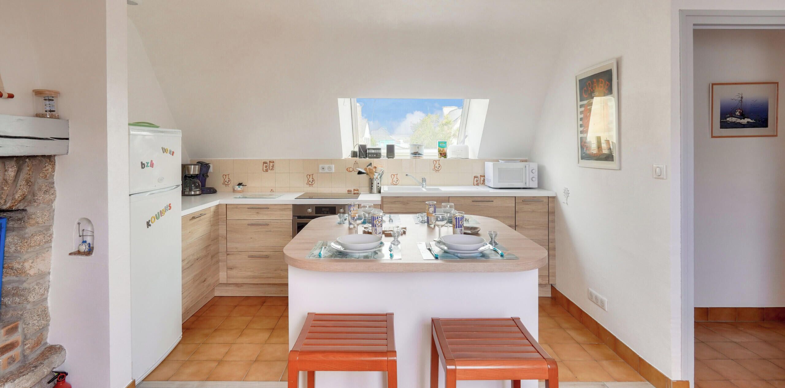 A compact kitchen with a central island, wooden cabinets, and a window providing natural light.