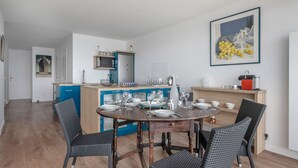 Una cocina moderna con comedor, que presenta una mesa de madera y sillas de mimbre, un armario azul y una obra de arte enmarcada en la pared.