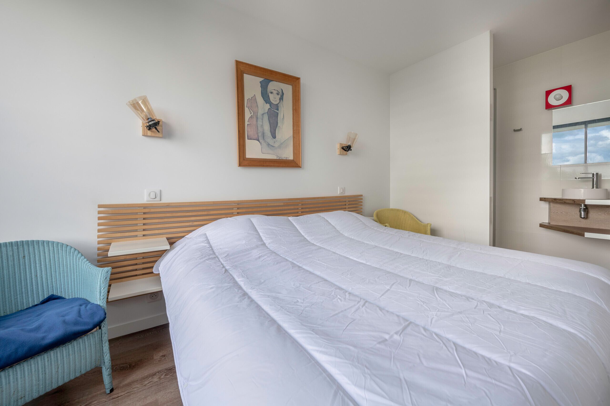 Une chambre d’hôtel moderne avec un grand lit, une tête de lit en bois, une chaise bleue et une petite table.