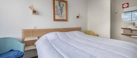 Une chambre d’hôtel moderne avec un grand lit, une tête de lit en bois, une chaise bleue et une petite table.