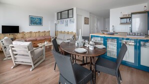 Una sala de estar moderna con un sofá, una mesa de comedor y sillas. Cuenta con una zona de cocina con armarios y un televisor.