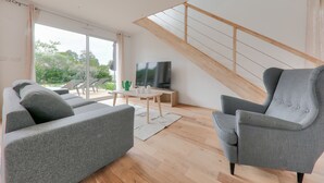 A modern living room with a grey sofa, a grey armchair, and a wooden staircase. - House for 8 - 300m from Rouvran beach (Le Tour-du-Parc)