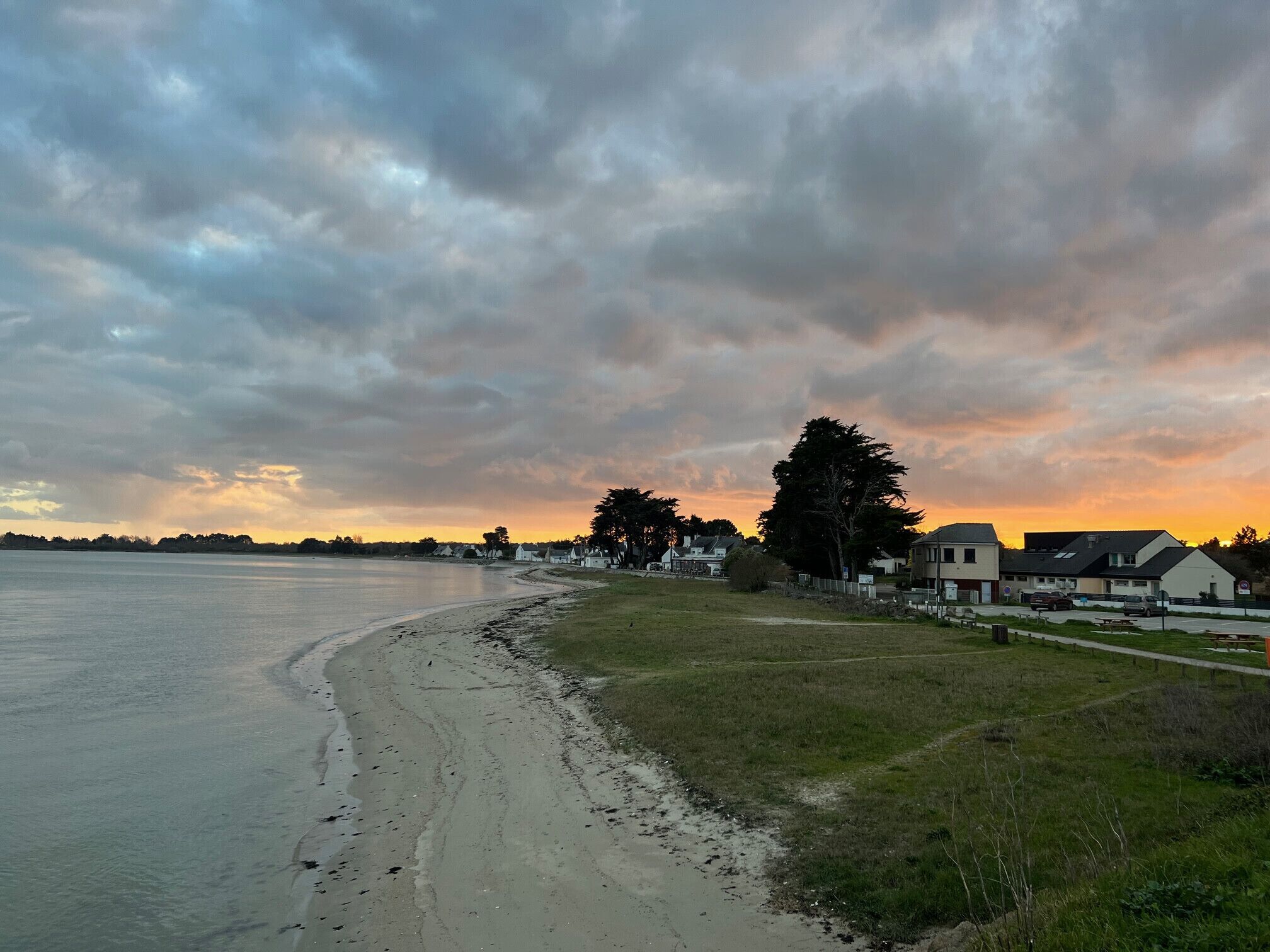 Una spiaggia con una riva sabbiosa, una zona erbosa e case sullo sfondo.