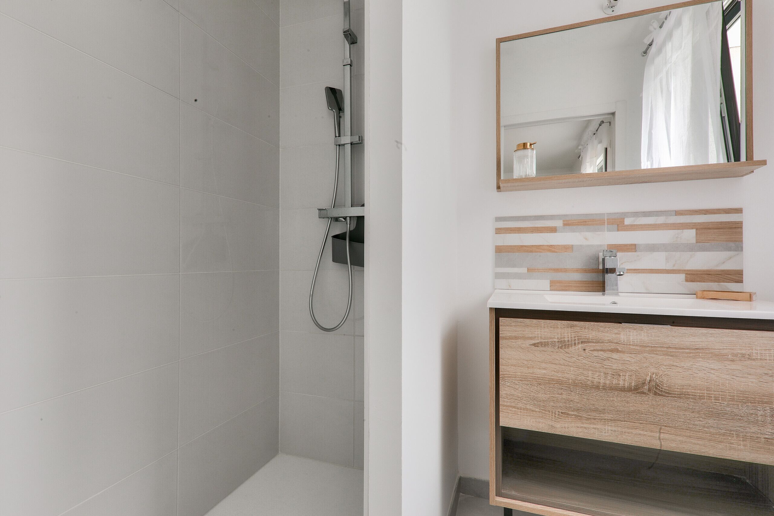 Un bagno moderno con doccia, un mobile vanitario in legno e uno specchio.