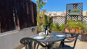 Une terrasse sur le toit, avec une table dressée pour deux personnes, entourée de chaises, et une vue sur le paysage urbain en arrière-plan.